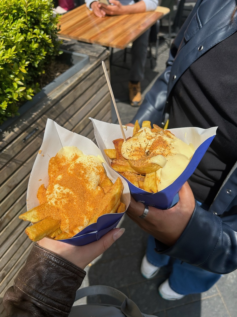 Two paper cones with fries topped with sauce