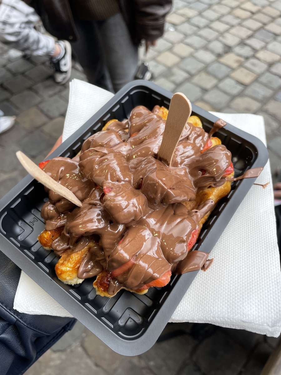 Two wooden forks stuck in belgian waffle with strawberries and nutella