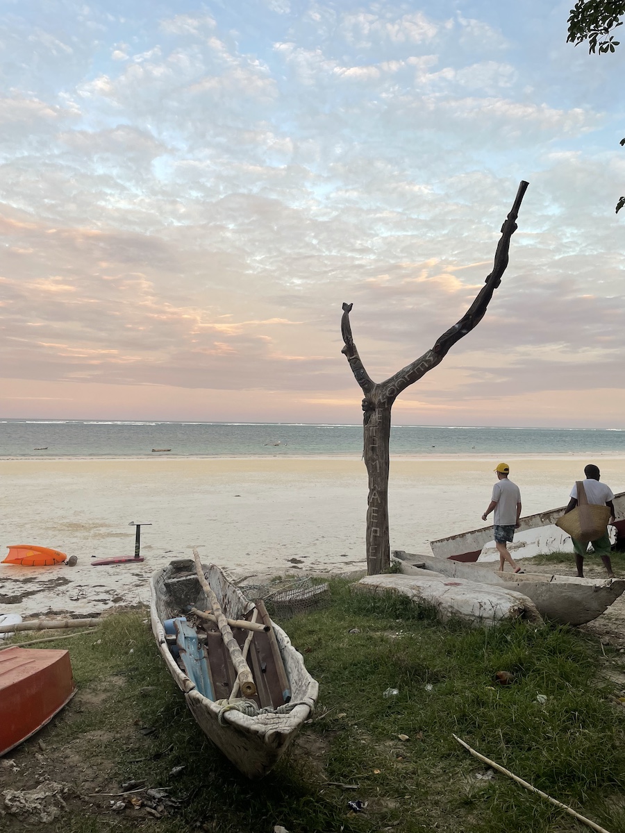 Pale pink sky over beach and water, a couple canoes flipped over on sand hump