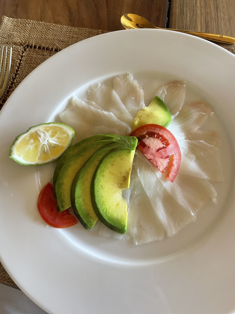 A plate of thinly cut fish with tomato and avocado