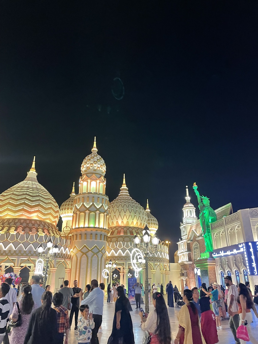 Yellow illuminated dome top building with green illuminated Statue of Liberty