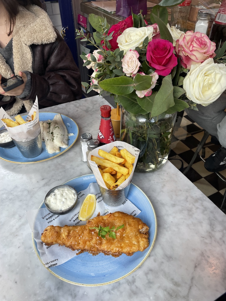 Fish and Chips on a plate next to a vase of pink and white roses