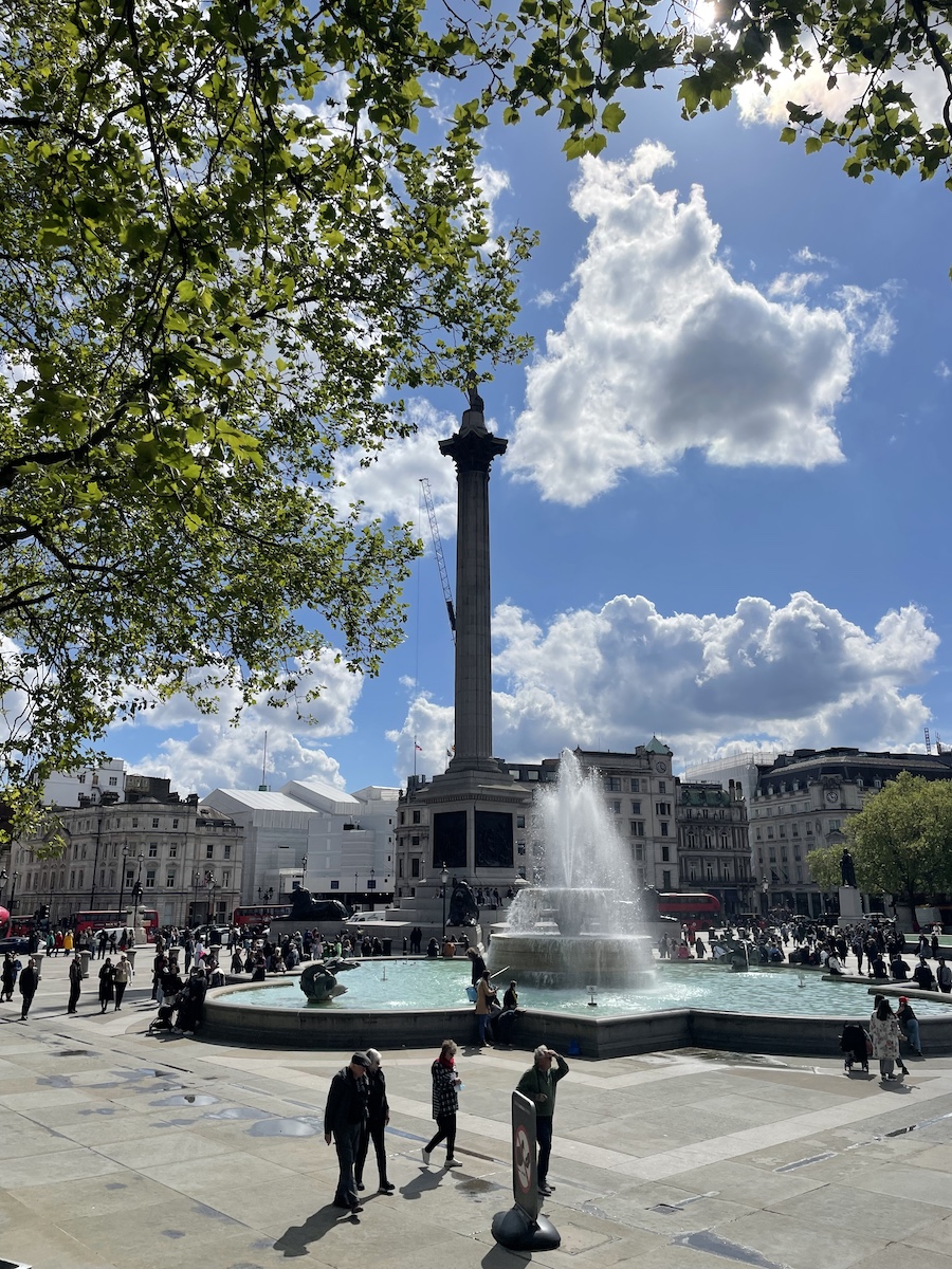 Fountain and pillar with statue in sunny day behind edge of a tree