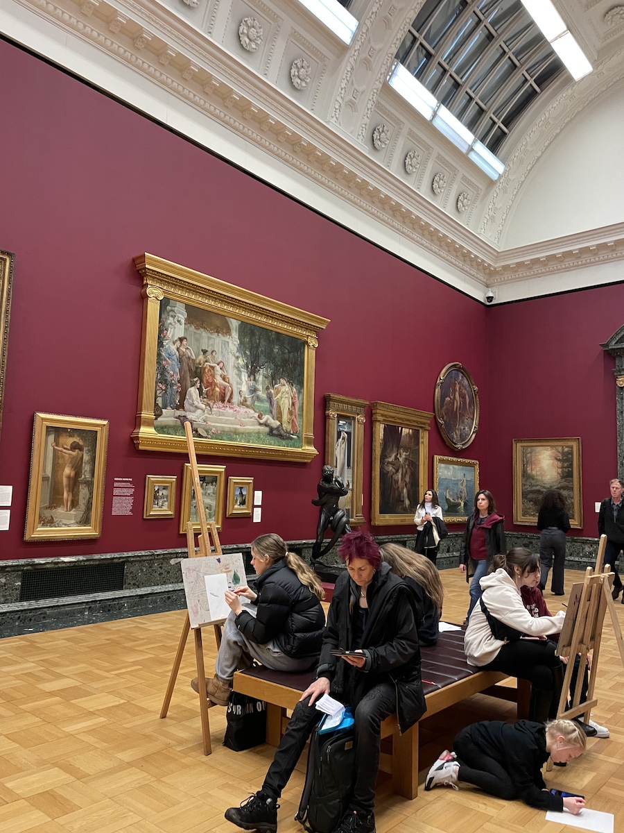4 people sitting on seat with art canvases hung on tall dark red walls