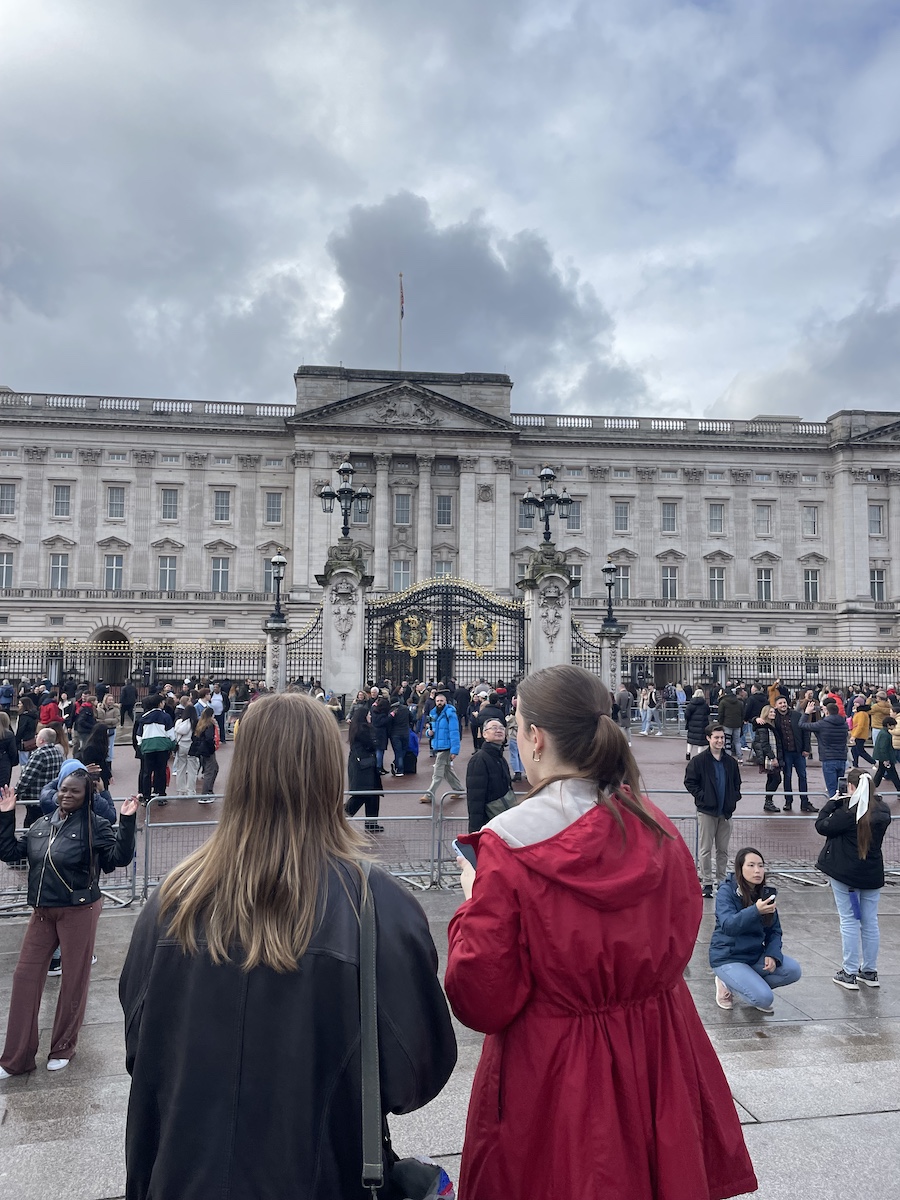Two girl's backs facing Buckingham Palace on cloudy sky day