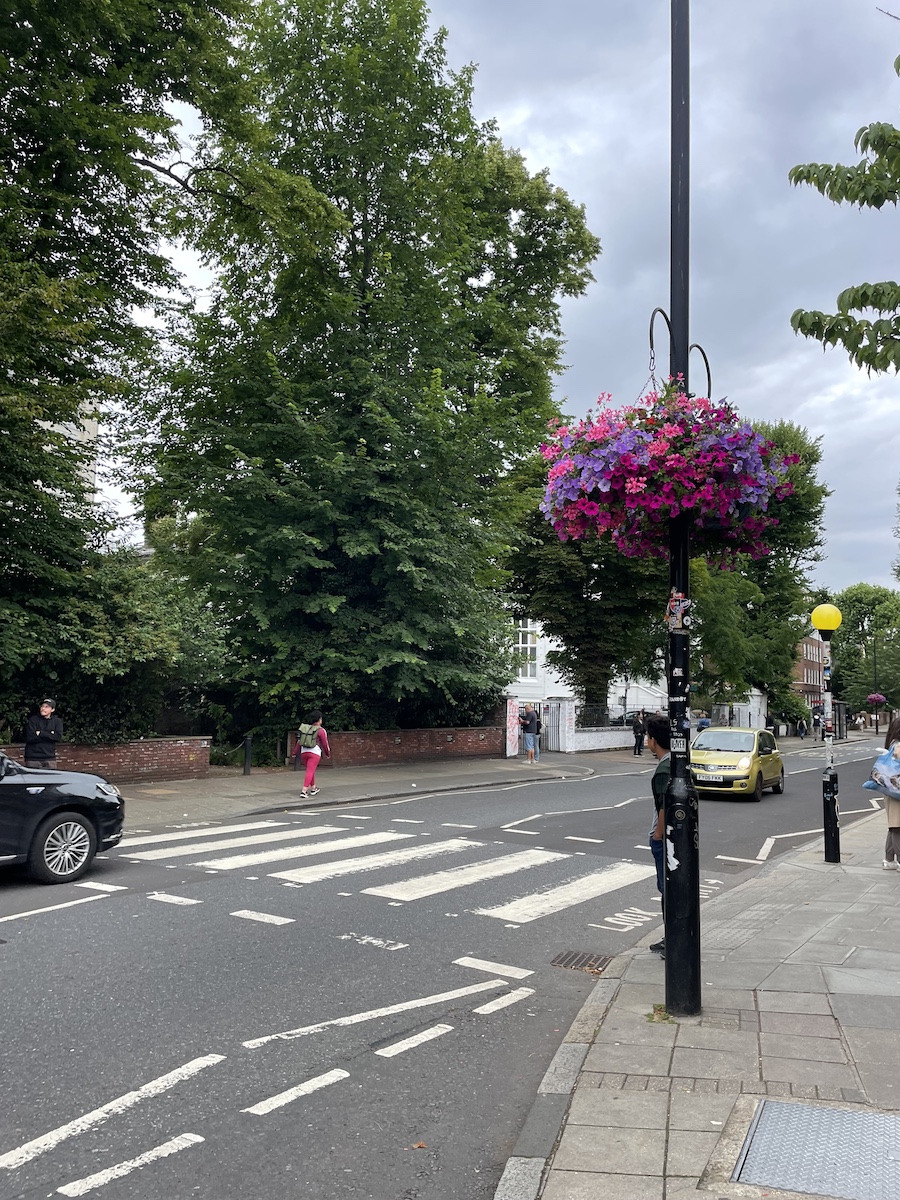People waiting to cross a crosswalk, with two cars passing by