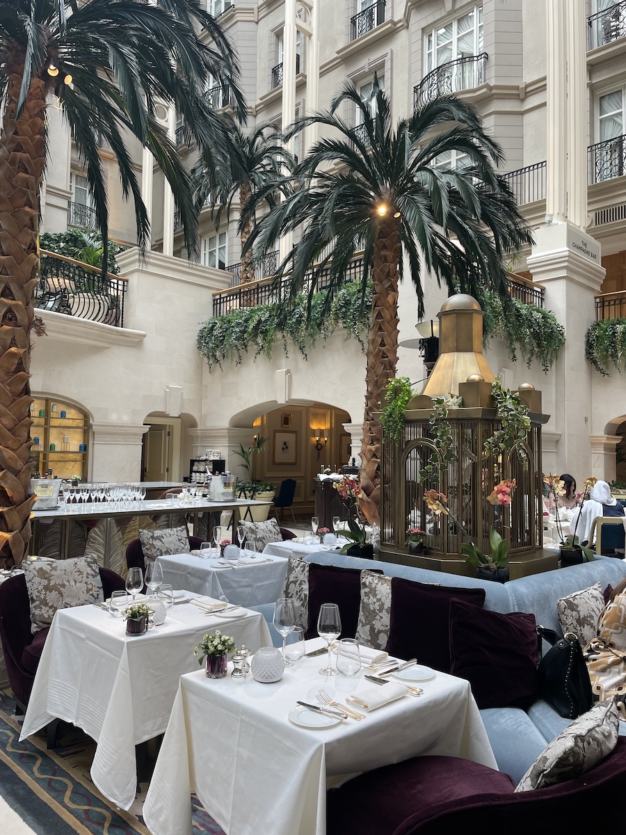 Fancy  tables and palm trees indoors, with hotel rooms surrounding