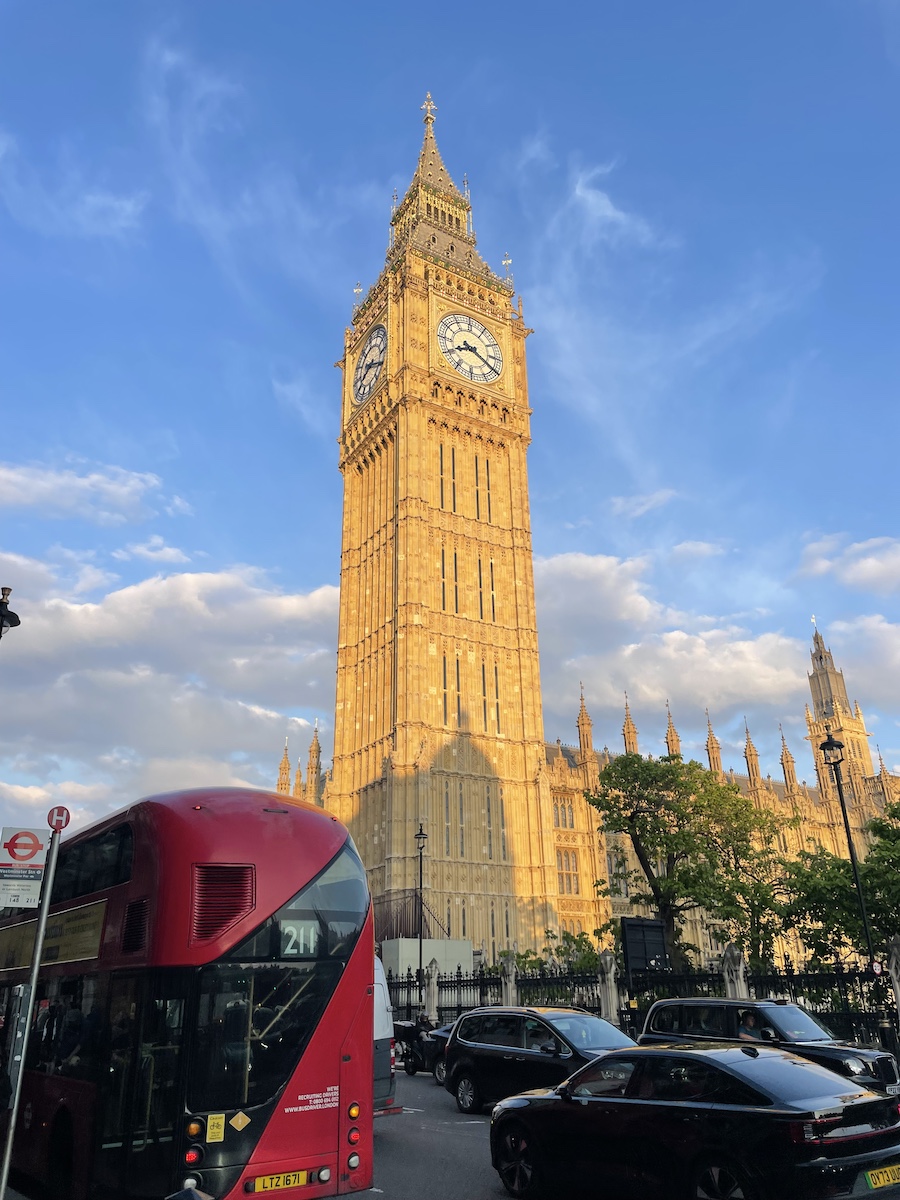 Upclose Big Ben in golden sun lighting, with view of red bus driving away